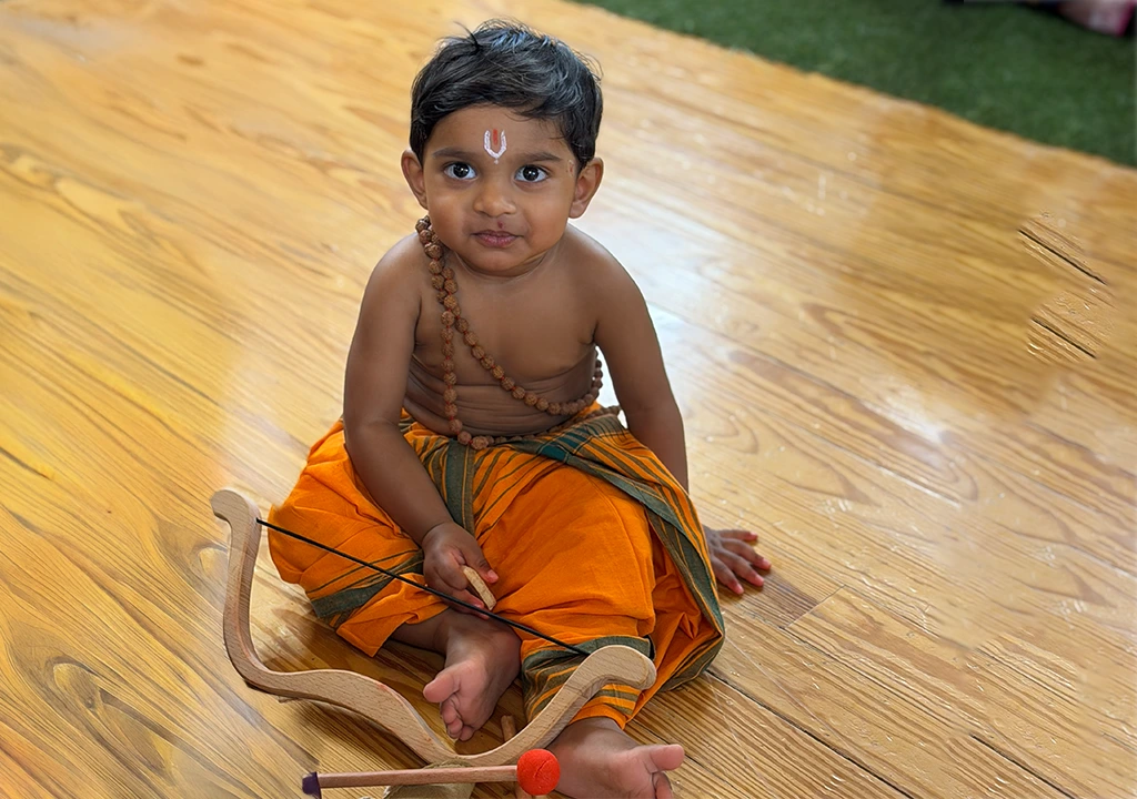A child dressed in traditional attire holding a small bow and arrow during a temple event.